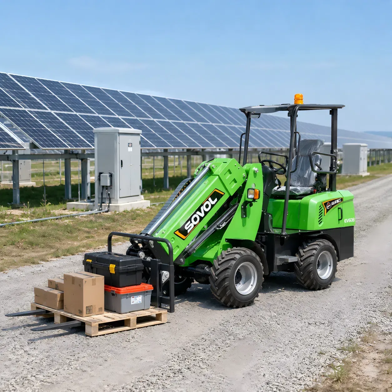 Chargeuse sur pneus électrique SOVOL SE906 utilisant un accessoire à fourche palettisée pour transporter des matériaux en carton et des outils le long d'une route de service de parc solaire, adaptée à un entretien propre et silencieux.