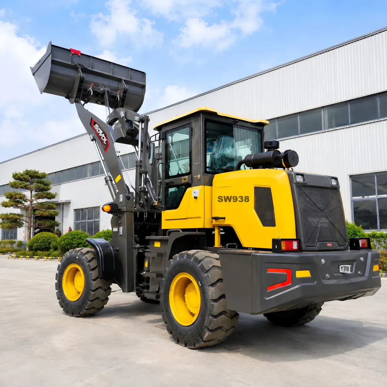 SOVOL SW938 1,5 ton tekerlekli yükleyicinin yükseltilmiş kepçeyle arka üç çeyrek görünümü, kapalı kabinini, güçlendirilmiş aks konfigürasyonunu ve pratik avlu taşıma tasarımını vurguluyor.
